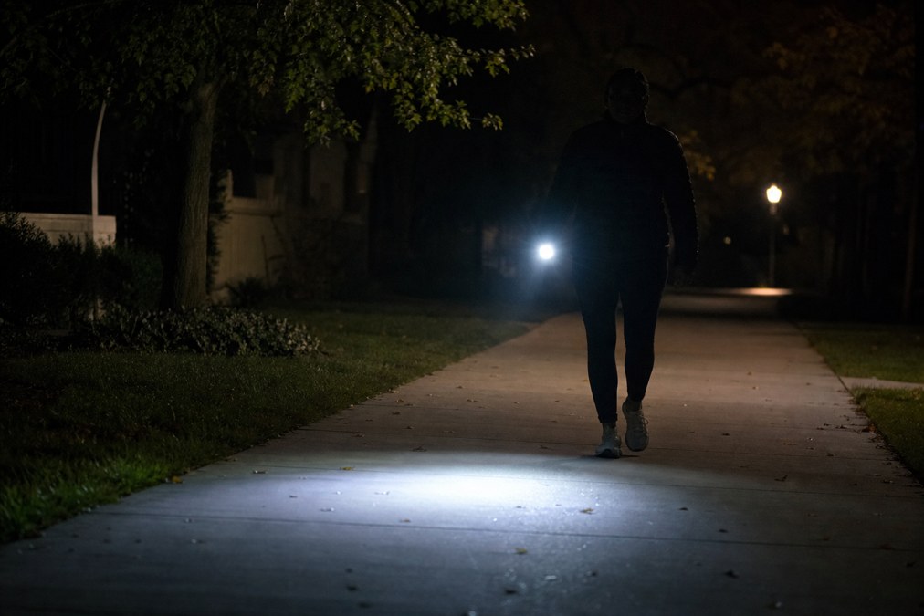 Bright handheld flashlight beam on a dark neighborhood walking path at night