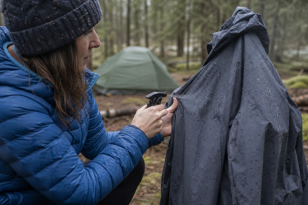 Spraying waterproof DWR treatment on a rain jacket outdoors